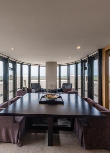 A meeting table and lounge area in a glass panelled room with view of the hills.