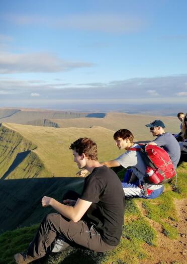 A group sitting on the top of a mountain looking at the views below.