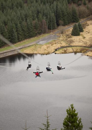 People travelling down a zip line over a reservoir amongst forestry.