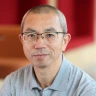 Close-up portrait of a person wearing glasses and a grey shirt against a blurred red background.
