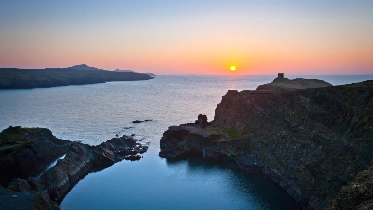 Sun setting on the still waters of the Blue Lagoon surrounded by cliffs.