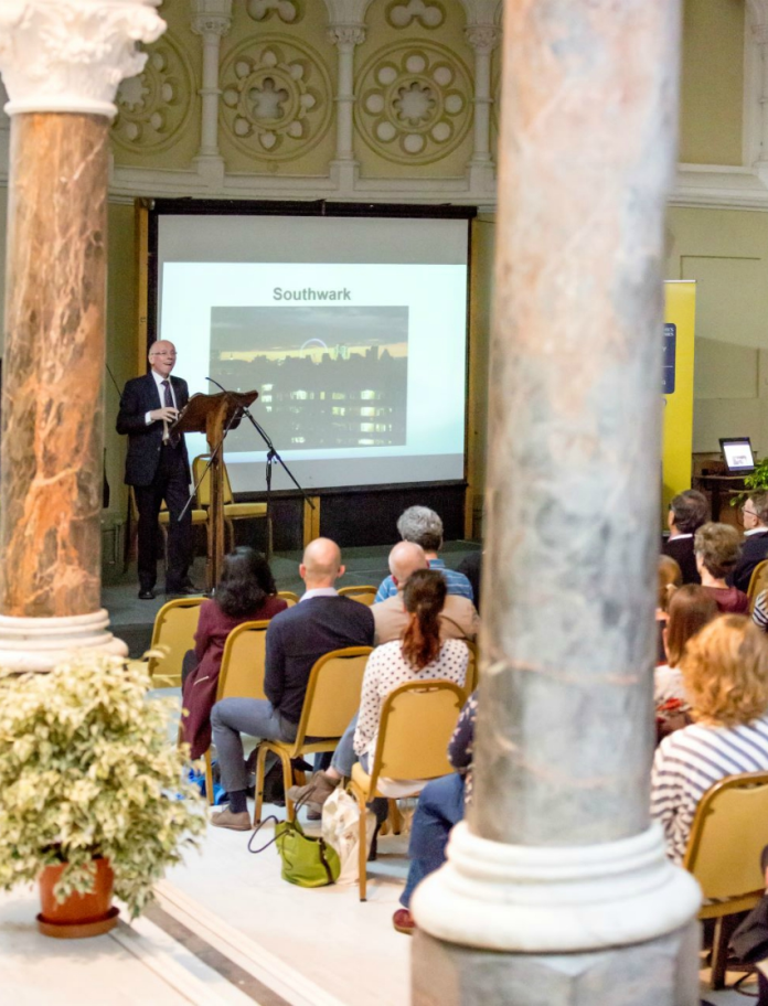 A group of people watching a presenter and screen in a university conference hall.