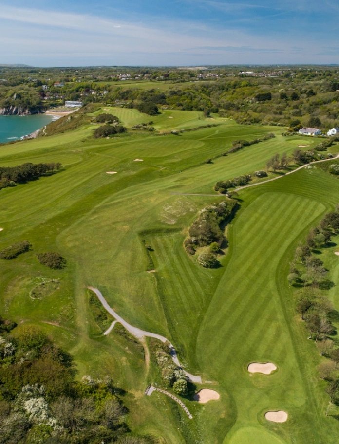 Aerial shot of a golf course and the blue waters of a bay alongside it.
