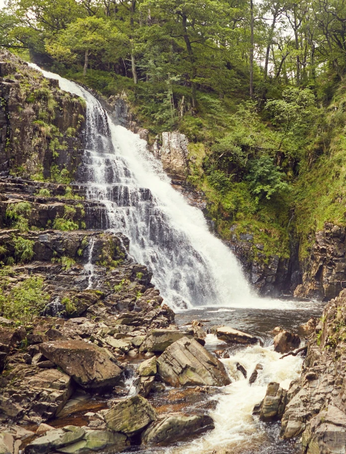Waterfall surrounded by rocks and greenery.