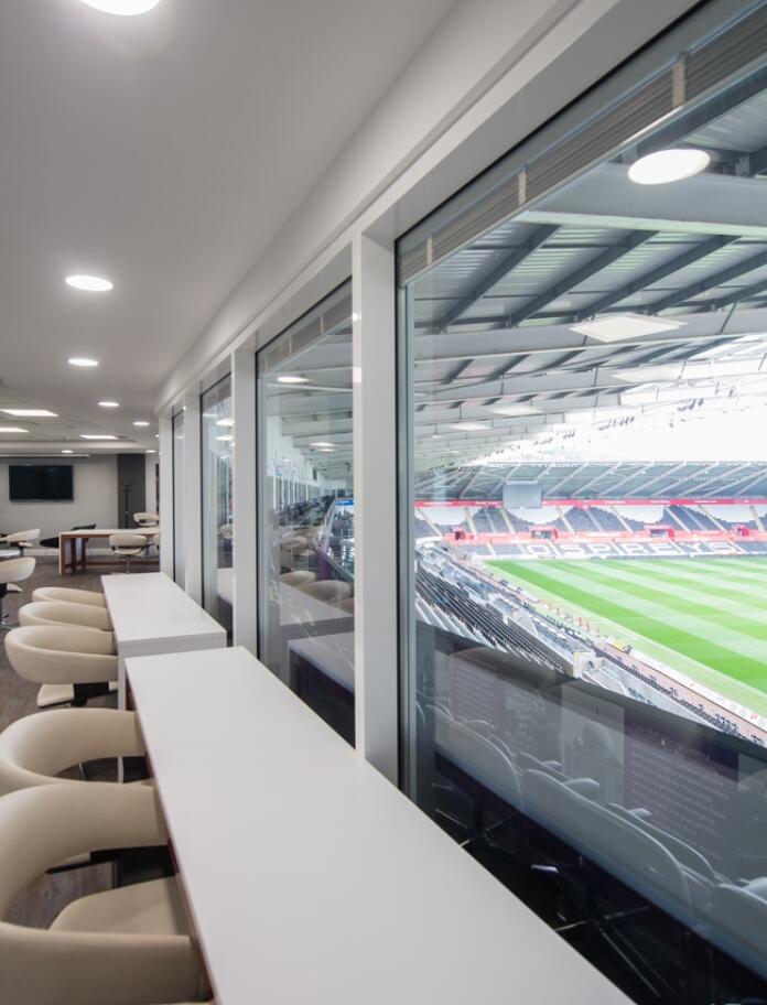 High white leather bar seats with white bar looking out of the stadium conference room towards the pitch 