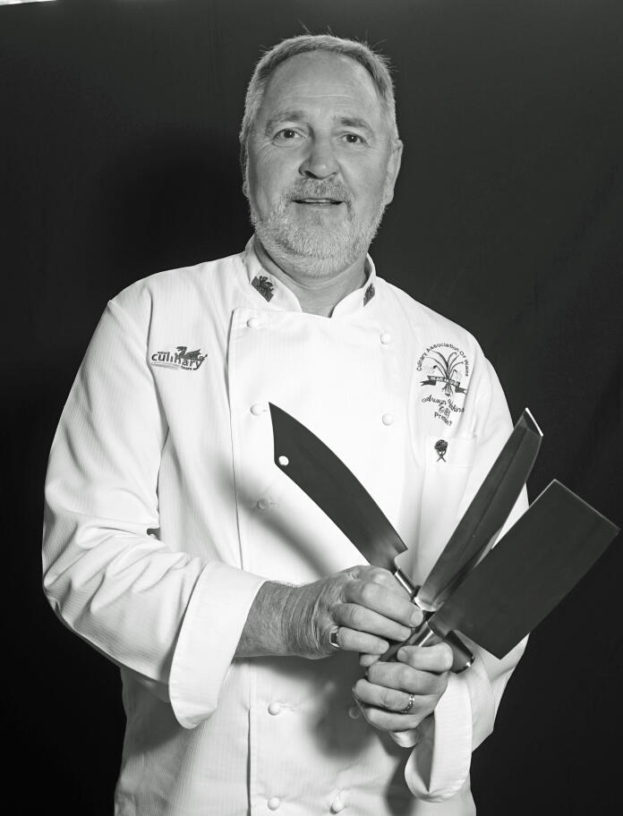 Black and White portrait image of Arwyn Watkins OBE with cooking knife set