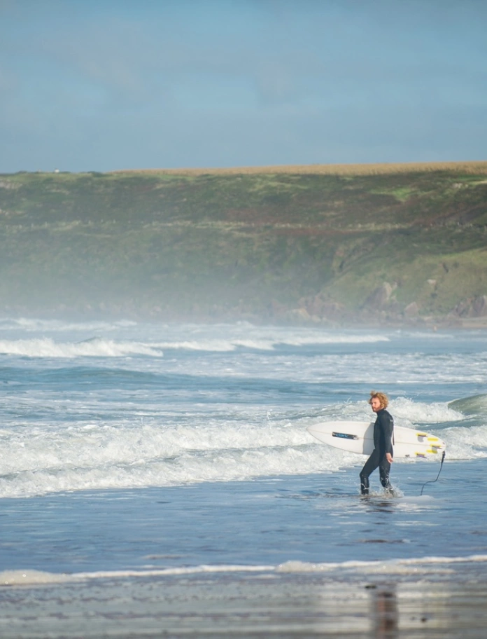 Surfer standing in teh blue shallow waters of teh sandy beach with waves crashing