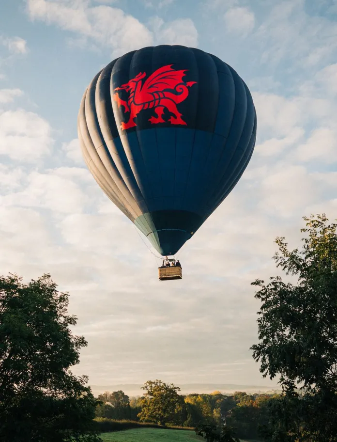 Hot air ballon flying over the Welsh Countryside with blue skies and green trees