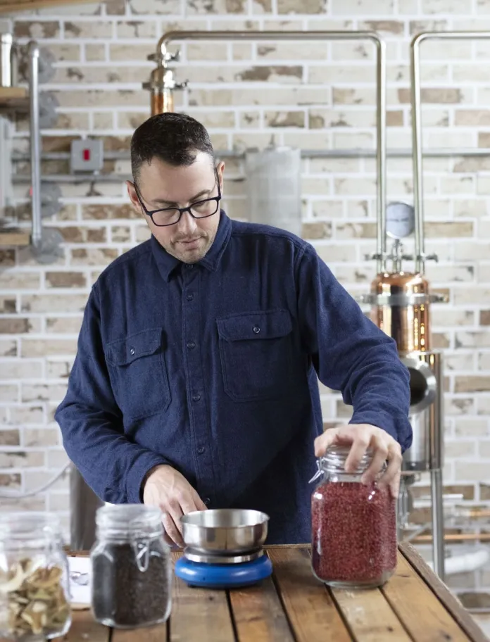 a person distilling with bottles on the table next to copper piping