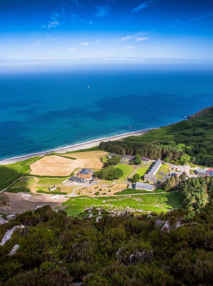 Aerial shot of Nant Gwrtheyrn surrounded by green landscape and the sea.
