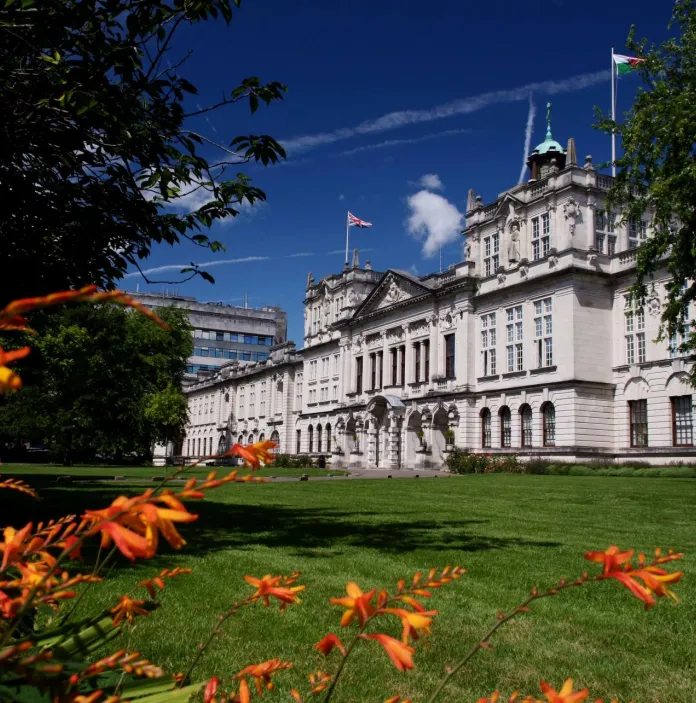 An external view of a university building framed by trees and flowers.