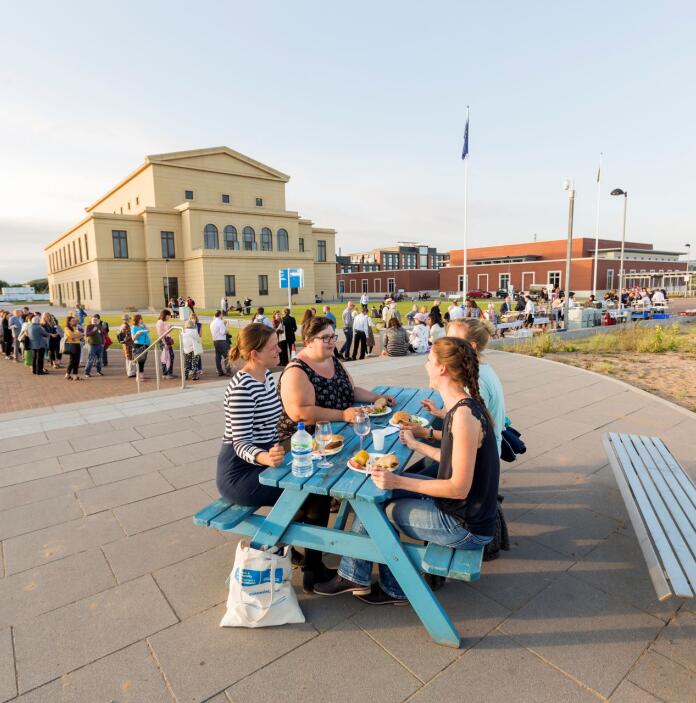 Delegates sitting on a picnic table enjoying a beach barbecue with the university in the background.