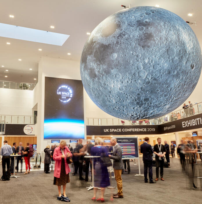 Delegates in an exhibition centre with a large moon hanging from the ceiling.