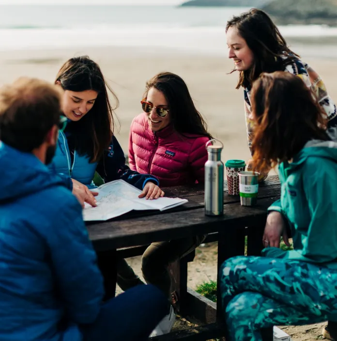 A group of people sitting on a park bench by the sea looking at a map.
