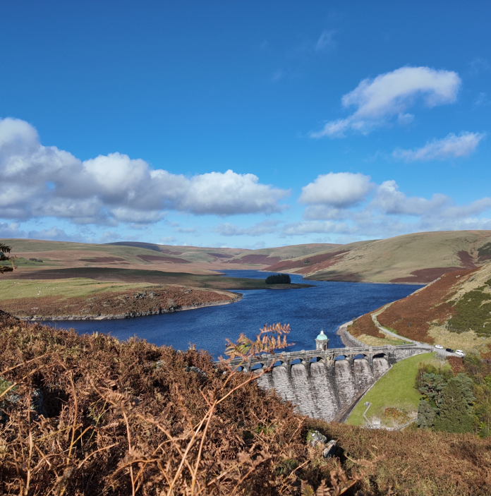 Elan Valley reservoir framed by rolling hills, a stone dam, and bright autumn sunlight