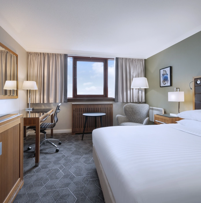 Bright, modern hotel room with a large bed, desk area, and a window overlooking the sky