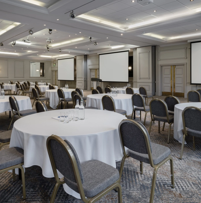 Spacious conference room set in cabaret style with round tables, chairs, and large presentation screens
