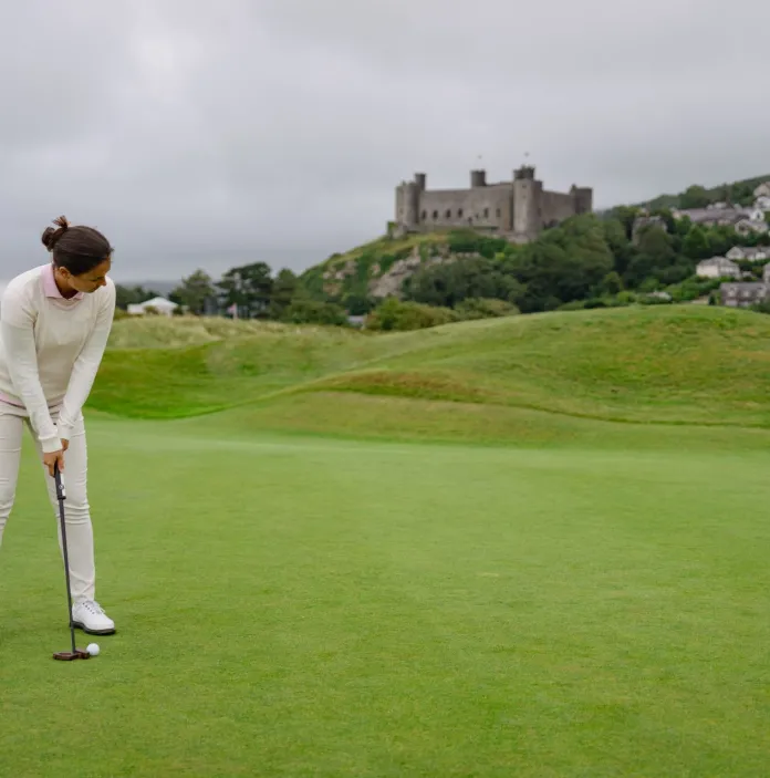 someone playing golf with views of a castle and mountains
