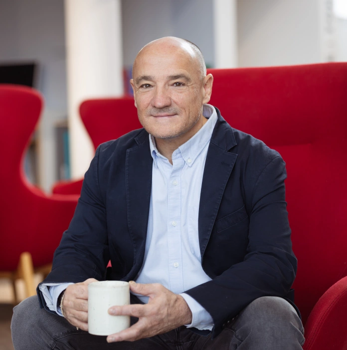 Bio image of Michael Brown holding white coffee mug and sat in red chair