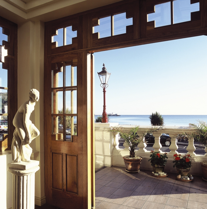 Open doorway leading to a terrace with sea views, potted plants, and a decorative statue inside.