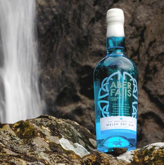 A blue bottle of Aber Falls welsh dry gin set against a waterfall.