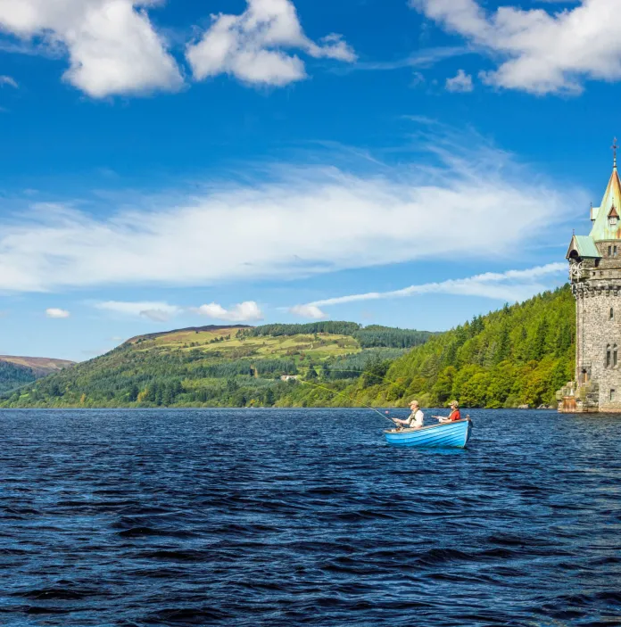 People fishing in a boat on a lake surrounded by a tower and mountains.