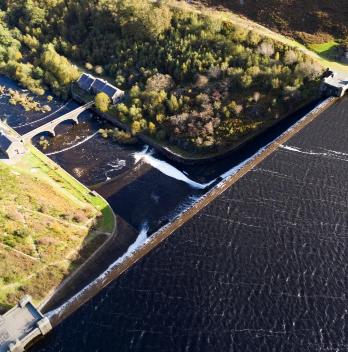 Arial shot looking onto the green trees, reservoir and dam.