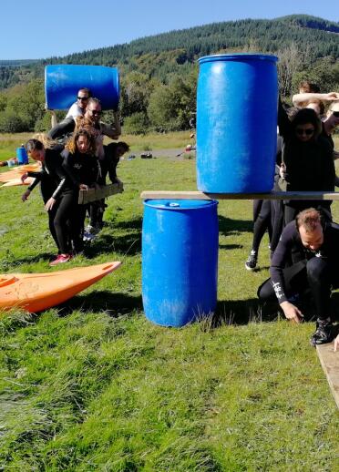 A group of people working as a team using planks, barrels and canoes.