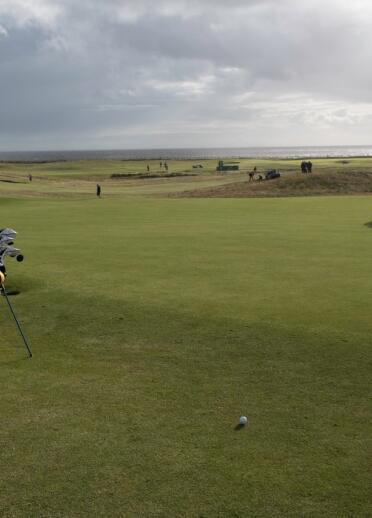 Golfers playing a round of golf with views of the sea.