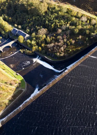 Arial shot looking onto the green trees, reservoir and dam.
