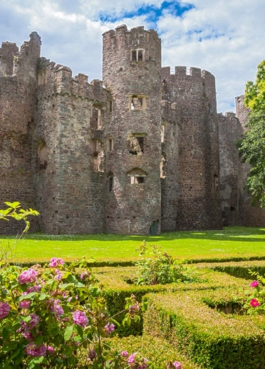 A grand castle by manicured green lawns, shrubs, flowers and trees.