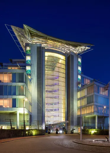 Night time image of the hotel with flags on the roundabout at the entrance and white lights in the suites and foyers.