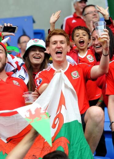 Group of people in Wales football shirts holding Welsh flag.