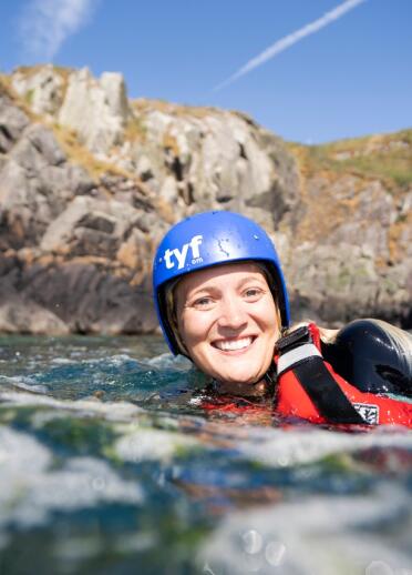 Woman in water smiling with TYF coasteering helmet and life jacket on 