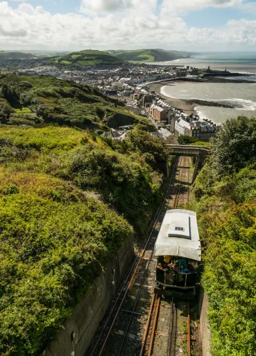 view of the tram going up the green grassy hill with Aberystwyth coastline in the background