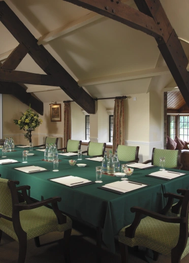 A spacious meeting room with a long conference table, green chairs, and exposed wooden beams.