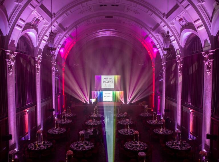 A hall in a university lit up with coloured lights and laid out with tables for a gala dinner.