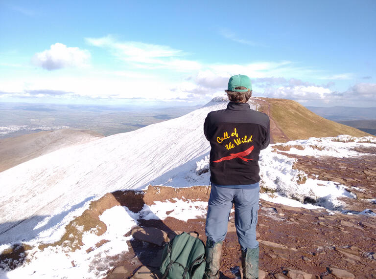 A man admiring the views on the top of a snow capped mountain.