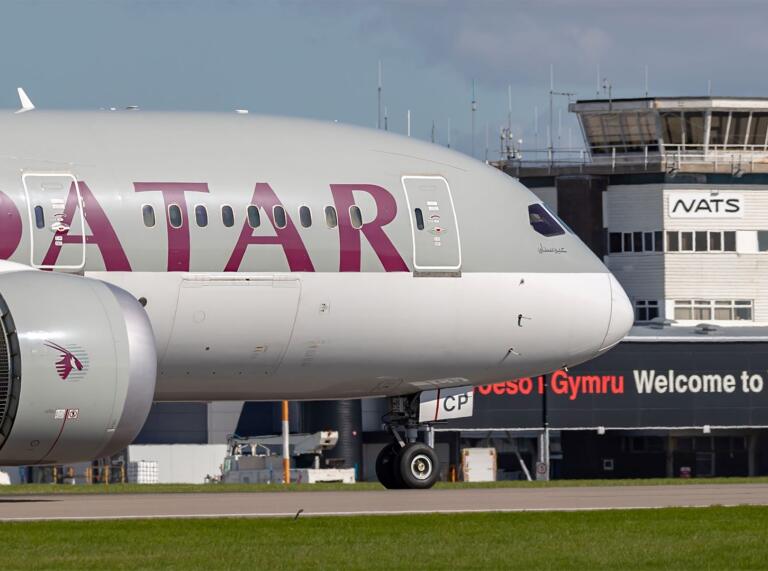 A large Qatar passenger plane arriving at Cardiff Airport next to a Welcome to Wales sign