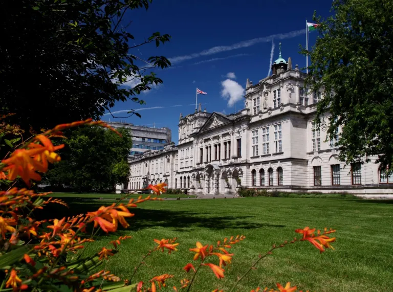 An external view of a university building framed by trees and flowers.