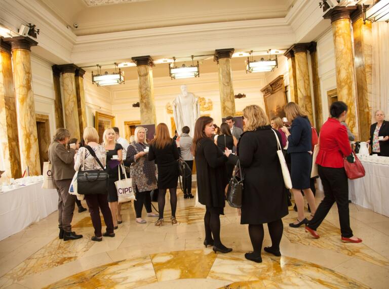 A group of people mingling and socialising in a grand hall with pillars.