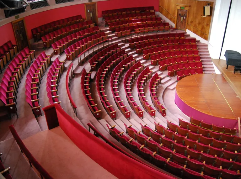 Chairs set out in an indoor amphitheathre looking onto a stage with a piano.