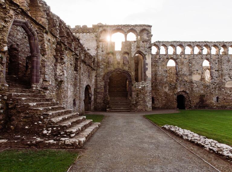 The sun setting and shining through the arches of a ruined bishops palace.