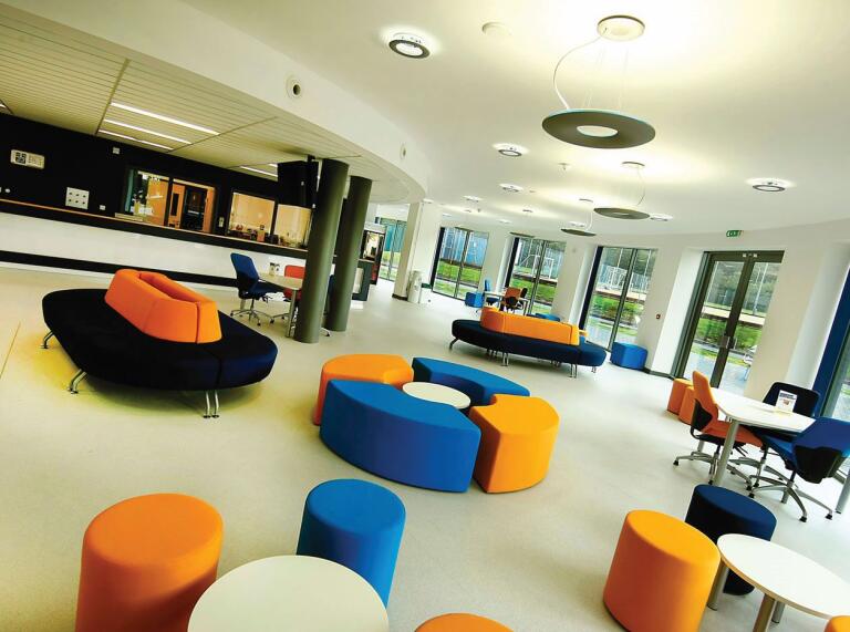 A foyer surrounded by large windows with colourful upholstered seats in a university.