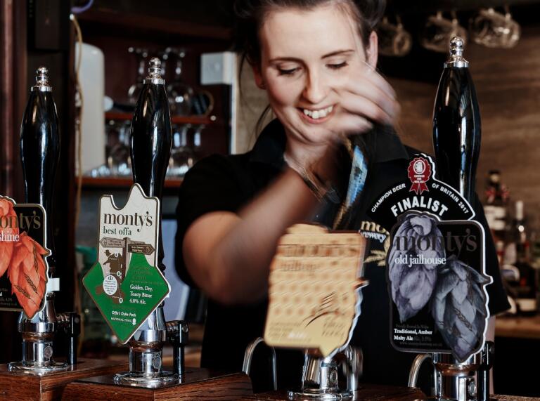 A lady smiling and pulling a pint at a bar.