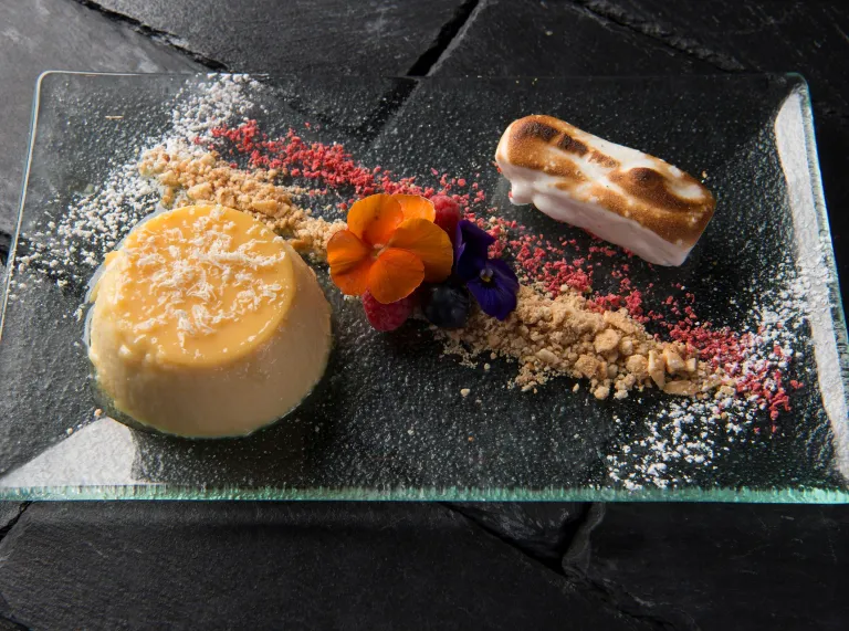 A dessert of panacotta, and meringue decorated with crumbs and flowers.