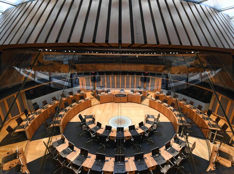 Chairs and tables set in a circle in the debating chamber of a parliament building.