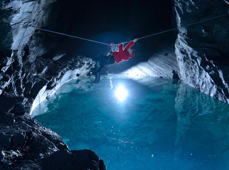 A climber on a zip wire in an underground cave over water