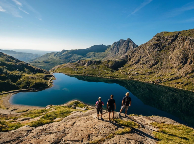 Three walkers looking across a lake at mountains in the background.