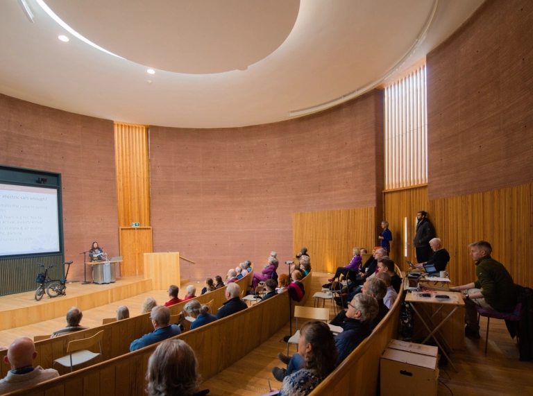 A theatre style meeting room with people looking on to a presenter and screen.